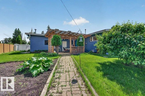 Rear exterior featuring a wood pergola over a patio, a paver walkway, a garden bed, and mature trees - 6916 92A Avenue, Edmonton, AB 
