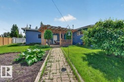 Rear exterior featuring a wood pergola over a patio, a paver walkway, a garden bed, and mature trees - 