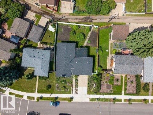 Aerial view of a residential property featuring a dark-shingled roof, an L-shaped footprint, and a front yard with landscaped garden beds - 6916 92A Avenue, Edmonton, AB 