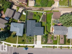 Aerial view of a residential property featuring a dark-shingled roof, an L-shaped footprint, and a front yard with landscaped garden beds - 