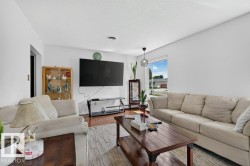 Spacious living area featuring light-toned walls, wood-finish flooring, a large window, a modern pendant light fixture, and a ceiling-mounted light fixture - 