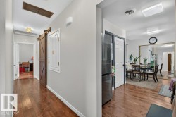 Hallway featuring rich wood-finish flooring, light grey painted walls, a sliding barn door, and recessed ceiling lighting - 