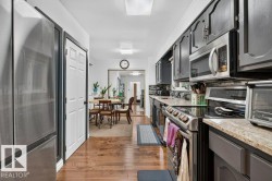 Galley kitchen featuring wood-finish flooring, stainless steel appliances, dark cabinetry, and light-toned countertops - 