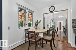 Kitchenette featuring a double casement window, mirrored closet doors, tile backsplash, wood-finish flooring, and baseboard heating - 