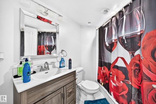 Bathroom featuring a wood-finish vanity with a white countertop and integrated sink, a large wall mirror, and a chrome-finish light fixture with three globe lights - 12410 171A Avenue, Edmonton, AB 
