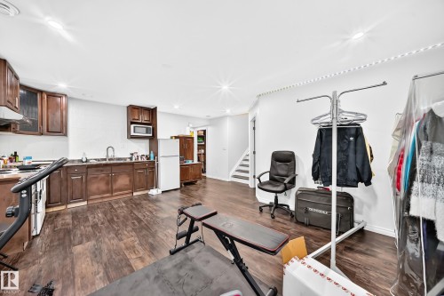 Spacious open-concept room featuring wood-finish flooring, a full kitchen with dark wood cabinetry and integrated appliances, recessed lighting, and a white color palette - 12410 171A Avenue, Edmonton, AB 