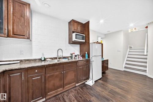 Kitchenette featuring rich brown cabinetry with ample storage, a double basin stainless steel sink, and a microwave - 12410 171A Avenue, Edmonton, AB 