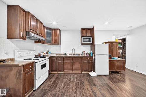 Kitchen featuring wood-finish flooring, white appliances, dark wood cabinetry, and laminate countertops - 12410 171A Avenue, Edmonton, AB 