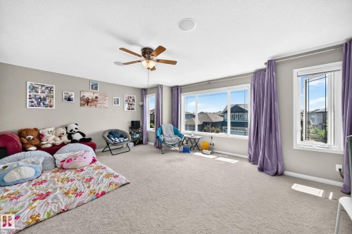 Spacious room featuring light gray wall paint, light-colored carpeting, a ceiling fan with light fixture, and multiple windows providing ambient light - 12410 171A Avenue, Edmonton, AB 