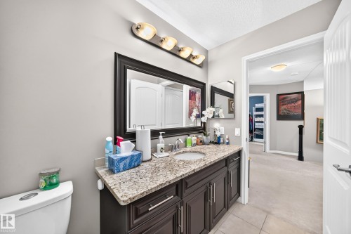 Bathroom vanity featuring a light-toned stone countertop with an undermount sink, dark wood-finish cabinetry, and a framed mirror - 12410 171A Avenue, Edmonton, AB 