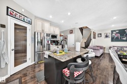 Open-concept kitchen featuring an island with a granite-style countertop, stainless steel appliances, light-toned cabinetry, and wood-finish flooring - 