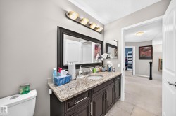 Bathroom vanity featuring a light-toned stone countertop with an undermount sink, dark wood-finish cabinetry, and a framed mirror - 