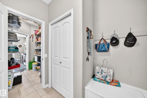 Utility area featuring light-toned tile flooring, a double-door closet with arch-top panels, and an open doorway revealing additional storage - 12410 171A Avenue, Edmonton, AB 