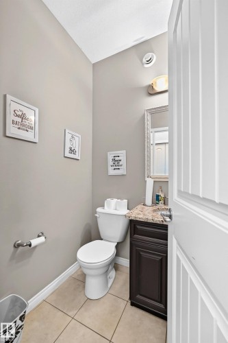Powder room featuring a white toilet, dark wood-finish vanity with a stone countertop, and an ornate framed mirror - 12410 171A Avenue, Edmonton, AB 