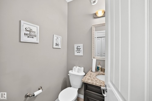 Bathroom featuring a white toilet, dark wood-finish vanity, granite-style countertop, and an ornate framed mirror - 12410 171A Avenue, Edmonton, AB 
