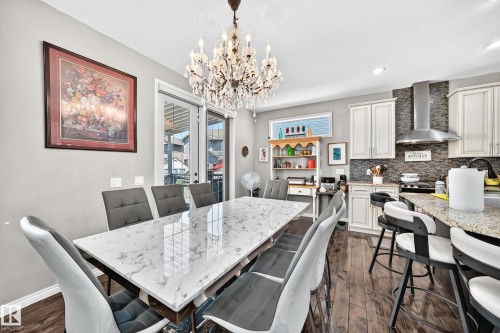 Open-concept dining and kitchen area featuring a crystal chandelier, wood-finish flooring, and white cabinetry - 12410 171A Avenue, Edmonton, AB 
