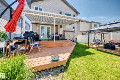 Expansive backyard featuring a multi-level wood-finish deck with a pergola, a manicured lawn, and white privacy fencing - 12410 171A Avenue, Edmonton, AB 