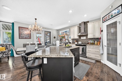 Kitchen featuring a central island with granite countertop and seating, stainless steel appliances, and wood-finish flooring - 12410 171A Avenue, Edmonton, AB 