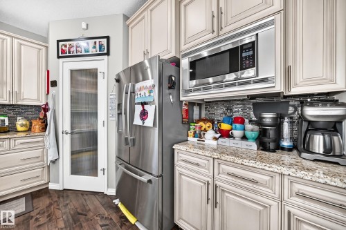 Kitchen featuring stainless steel appliances, granite countertops, wood-finish flooring, a glass-paneled pantry door, and full-height cabinetry - 12410 171A Avenue, Edmonton, AB 