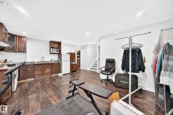 Spacious open-concept room featuring wood-finish flooring, a full kitchen with dark wood cabinetry and integrated appliances, recessed lighting, and a white color palette - 