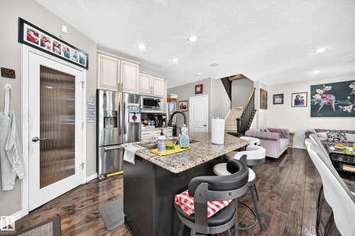 Open-concept kitchen featuring an island with a granite-style countertop, stainless steel appliances, light-toned cabinetry, and wood-finish flooring - 12410 171A Avenue, Edmonton, AB 