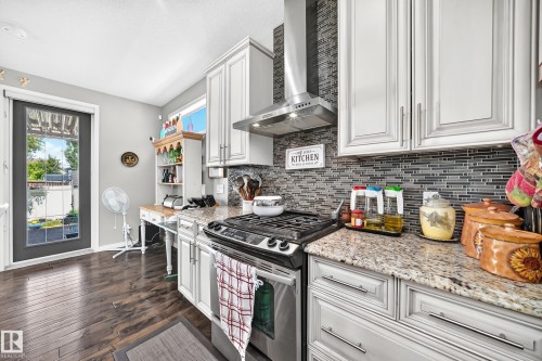 Kitchen featuring wood-finish flooring, shaker-style cabinetry, granite countertops, and a full tile backsplash - 12410 171A Avenue, Edmonton, AB 