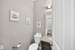 Bathroom featuring a white toilet, dark wood-finish vanity, granite-style countertop, and an ornate framed mirror - 