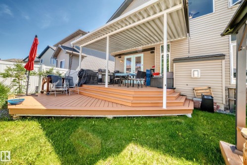 Expansive backyard featuring a multi-level wooden deck with integrated steps, a white slatted patio cover, and dual glass French doors - 12410 171A Avenue, Edmonton, AB 