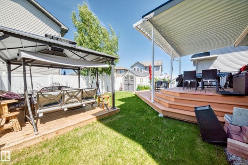 Expansive backyard featuring a tiered wood deck with an attached covered patio, a secondary wood deck with a gazebo, a green lawn, and a gray storage shed - 12410 171A Avenue, Edmonton, AB 