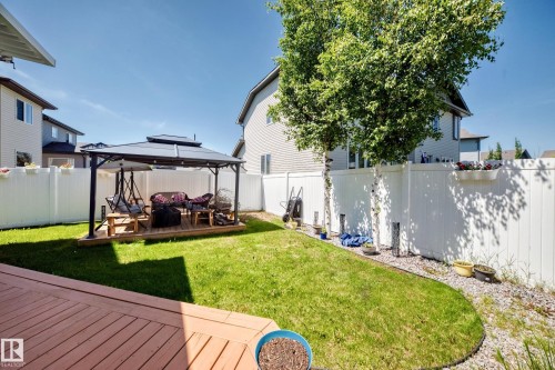 Expansive backyard featuring a large wooden deck, a gazebo with a built-in wooden platform, a manicured lawn, and white privacy fencing - 12410 171A Avenue, Edmonton, AB 