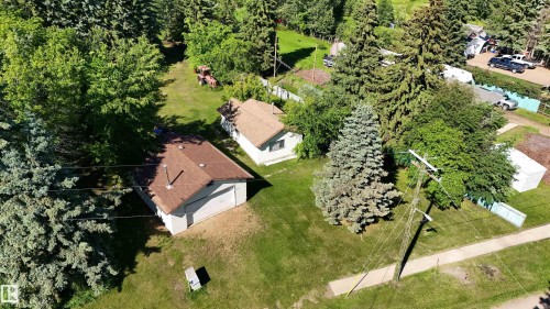 Expansive property featuring a detached garage with a brown shingle roof, a secondary structure with a matching roof, a broad grassy lawn, and mature evergreen and deciduous trees - 5416 51 Avenue, Andrew, AB 
