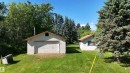 White-sided garage structure with a single bay door and a second white-sided building set on a grassy lot - 5416 51 Avenue, Andrew, AB 