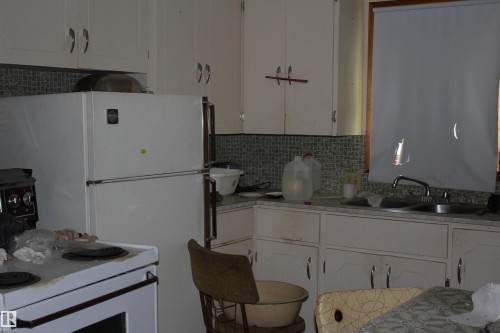 Kitchen featuring white cabinetry, tile backsplash, laminate countertops, and a window with a roller blind - 5416 51 Avenue, Andrew, AB - Indoor Photo Showing Kitchen With Double Sink