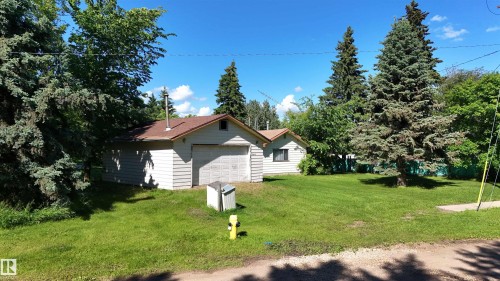 Detached garage with horizontal siding, a shingled roof, and an overhead door, surrounded by mature trees and a substantial lawn - 5416 51 Avenue, Andrew, AB 