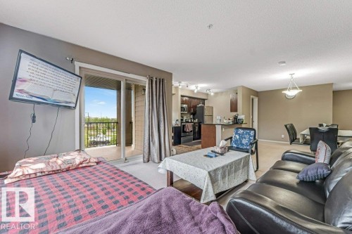 Open-concept living area featuring a sliding glass door to a private balcony, a kitchen with dark cabinetry and stainless steel appliances, and an adjacent dining area with a contemporary chandelier - 225 111 Watt Common, Edmonton, AB 