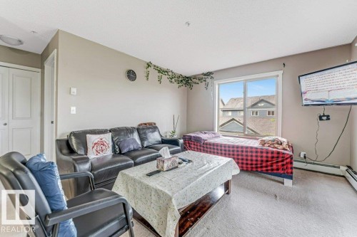 Living space featuring light neutral wall paint and carpeting, dual bi-fold closet doors, and an expansive window with white trim - 225 111 Watt Common, Edmonton, AB 