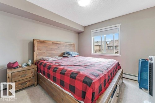 Carpeted bedroom featuring a large window with white trim, neutral wall paint, and a built-in valance - 225 111 Watt Common, Edmonton, AB 