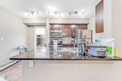 Kitchen featuring an expansive stone-finish countertop with an undermount sink, dark wood-finish cabinetry, and stainless steel appliances including a refrigerator and microwave - 