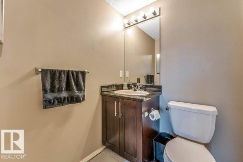 Powder room featuring a dark wood-finish vanity with a stone-finish countertop, undermount sink, and wall-mounted mirror with overhead lighting - 225 111 Watt Common, Edmonton, AB 