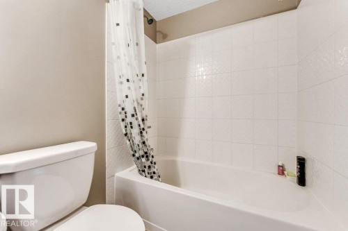 Full-size bathtub with white tile surround featuring a subtle geometric pattern - 225 111 Watt Common, Edmonton, AB 