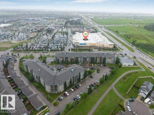 Aerial perspective showcasing the residential buildings with multiple levels, surrounding green spaces, and surface parking areas - 225 111 Watt Common, Edmonton, AB 