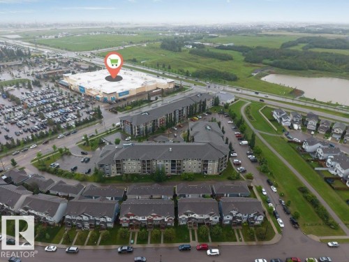 Aerial perspective showcasing a large commercial retail building with extensive parking, multi-story residential buildings, and rows of townhouses - 225 111 Watt Common, Edmonton, AB 