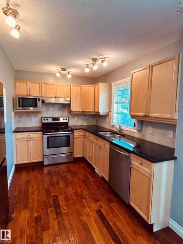 Kitchen featuring a full suite of stainless steel appliances, dark countertops, light wood cabinetry, and wood-finish flooring - 89 12050 17 Avenue, Edmonton, AB 