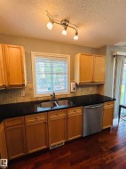 Kitchen featuring wood-finish flooring, light wood cabinetry, black countertops, and a stainless steel double basin sink with a matching faucet - 