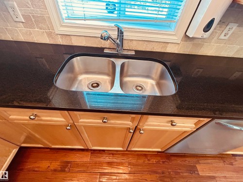 Under-mount stainless steel double basin sink with a chrome faucet set into a dark countertop, complemented by a tiled backsplash - 89 12050 17 Avenue, Edmonton, AB 
