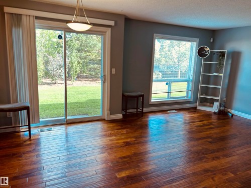 Spacious room featuring rich wood-finish flooring, a sliding glass door providing direct outdoor access, a large secondary window, and a contemporary ceiling light fixture - 89 12050 17 Avenue, Edmonton, AB 