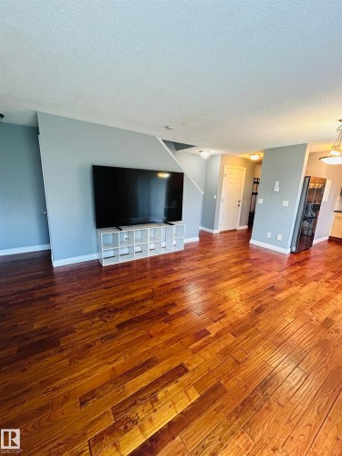 Rich wood-finish flooring extending through an open-concept living area - 89 12050 17 Avenue, Edmonton, AB 