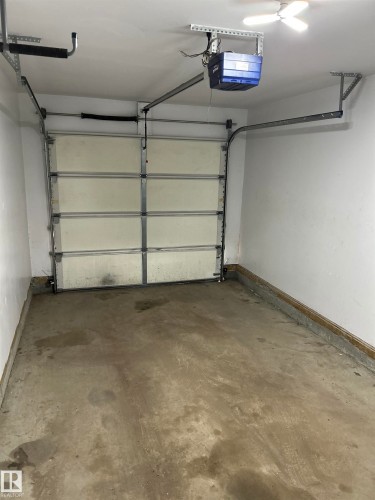 Single-car garage featuring a sectional overhead door with an automatic opener, concrete flooring, and overhead lighting - 89 12050 17 Avenue, Edmonton, AB 