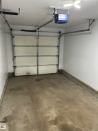 Single-car garage featuring a sectional overhead door with an automatic opener, concrete flooring, and overhead lighting - 