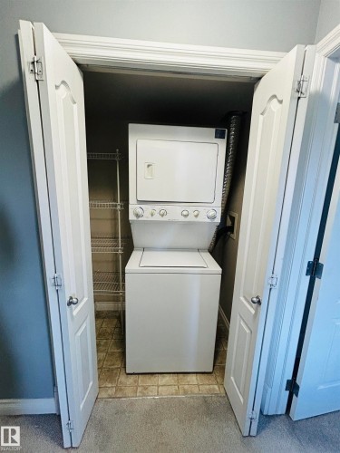 Dedicated laundry closet featuring a white stacked washer and dryer unit, tile flooring, and integrated wire shelving - 89 12050 17 Avenue, Edmonton, AB 